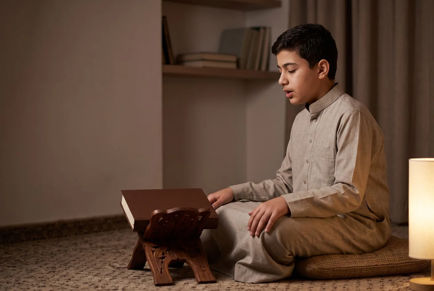 A young man reciting from memory with his eyes closed, a closed mushaf resting in front of him.